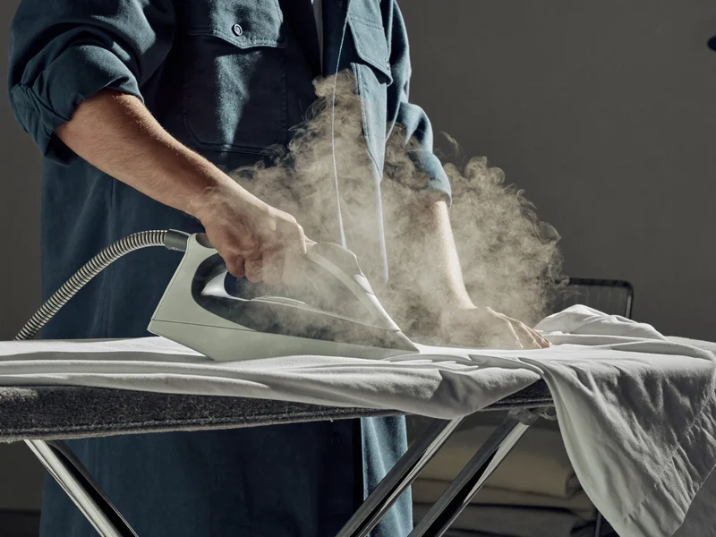 Mains d'un opérateur repassant une chemise blanche à la vapeur sur table aspirante