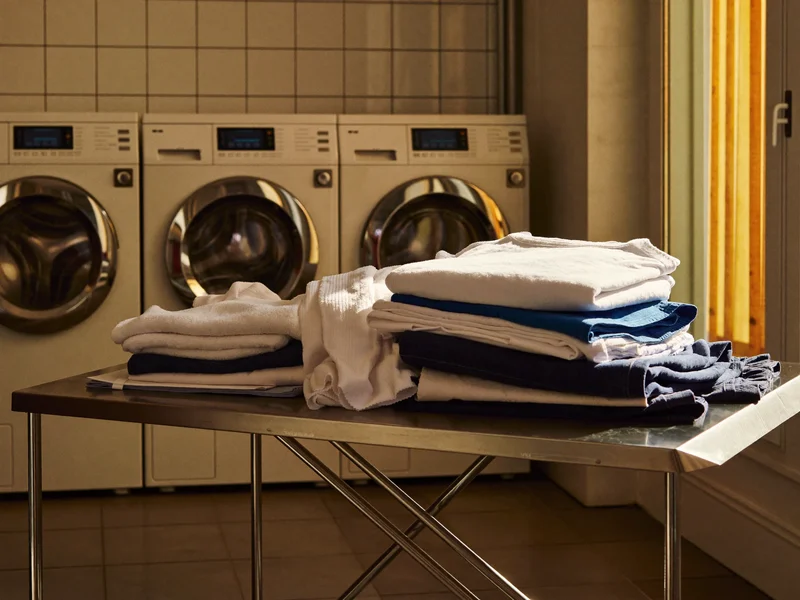 Piles de linge courant plié sur table inox, à côté de lave-linge industriels