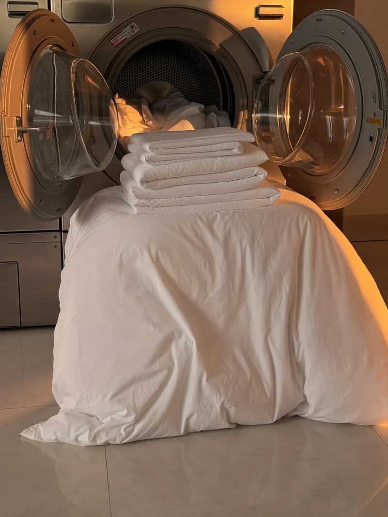 Couette blanche pliée et linge de lit près d'un tambour de lave-linge ouvert